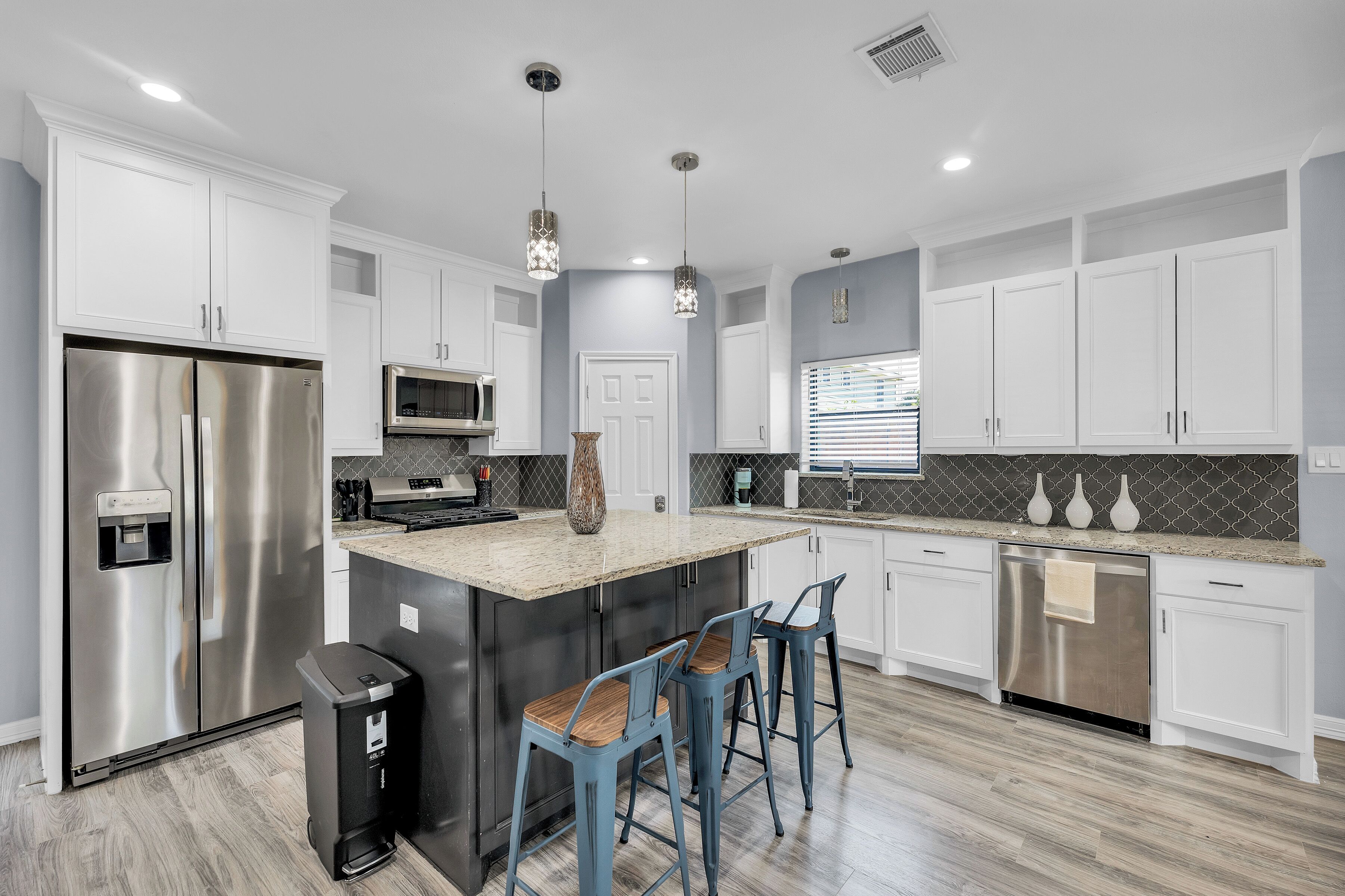A modern kitchen with white cabinets, stainless steel appliances, a granite countertop, and blue bar stools.
