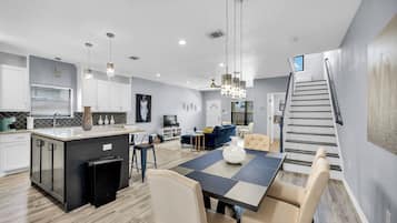 A modern kitchen with a central island, dining area with a table and chairs, and a staircase leading to an upper level.