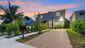 A modern two-story house with a brick pathway leading to the entrance, surrounded by well-maintained greenery and palm trees. - Miami 4BR Family Home | Patio + Parking (Miami)