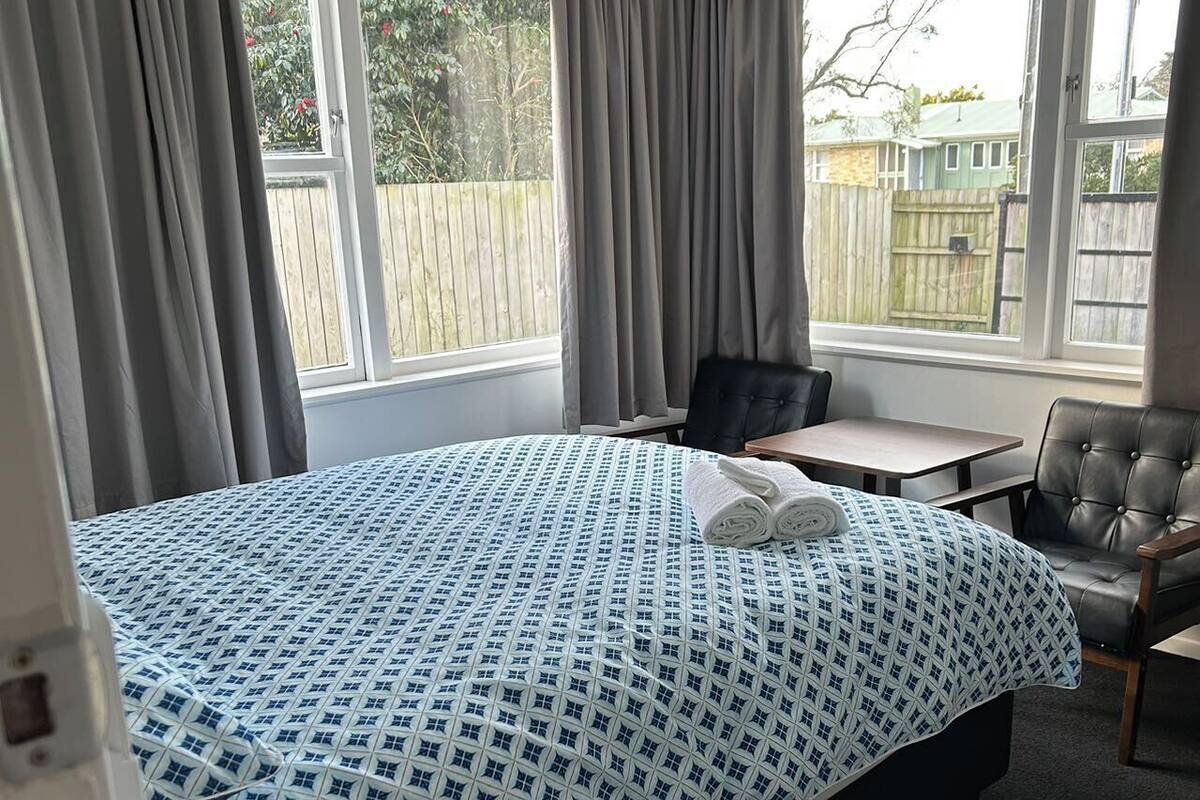 A bedroom with a bed, a desk, a chair, and a window with curtains.