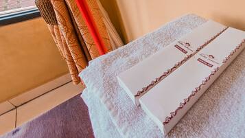 A stack of white towels with red borders on a textured surface, possibly a bed or a counter.