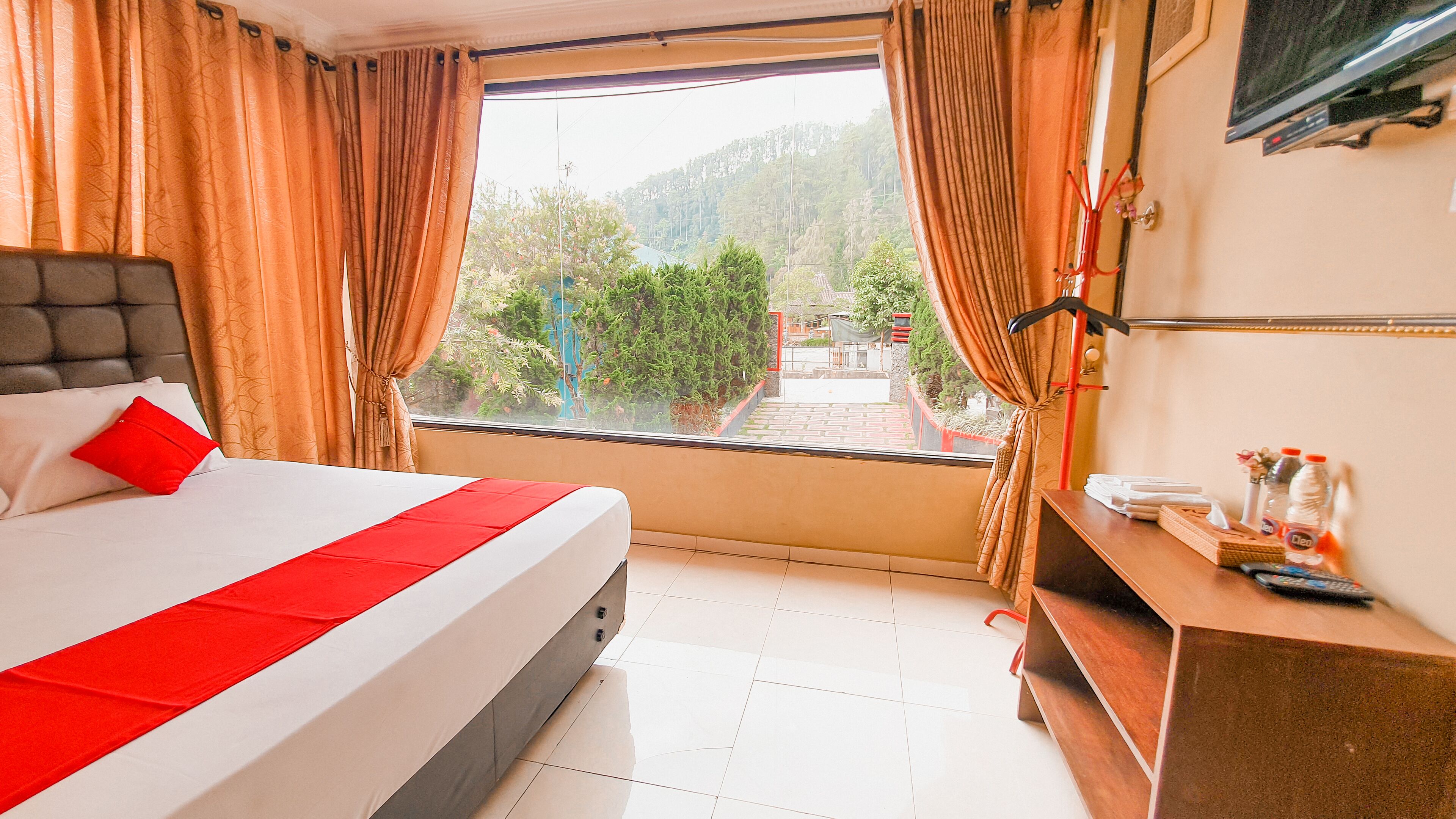 Ein Hotelzimmer mit Bett, Vorhängen, Fenster und Schreibtisch mit Fernseher und Fernbedienung.