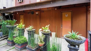 A building with a wooden door labeled "102" and a series of planters with various plants in front. - Red Chilies Hill Hotel (Tawangmangu)