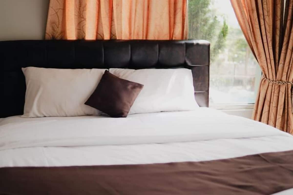 Una cama con almohadas blancas y marrones, cabecera negra y cortinas color beige.