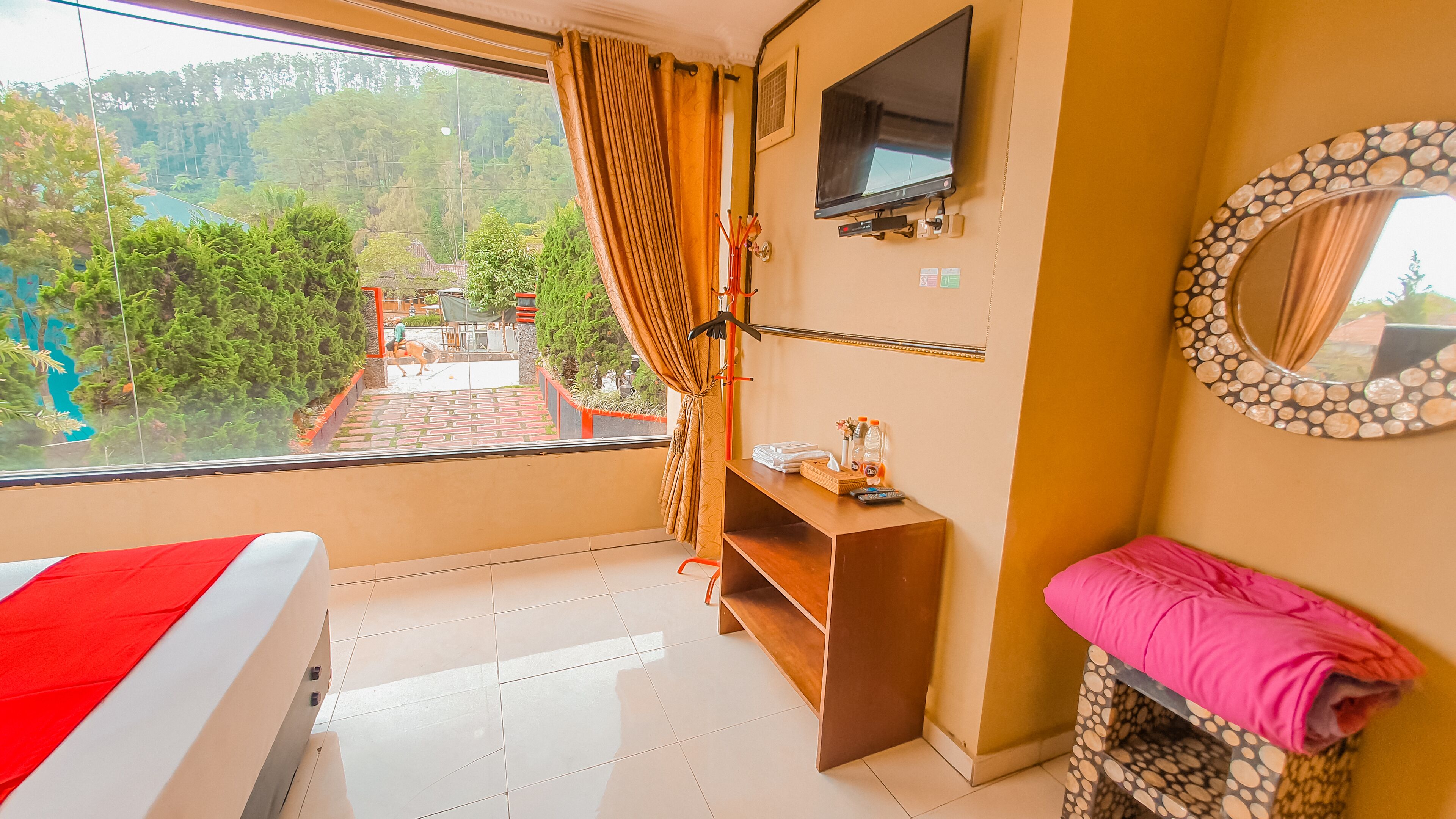 A hotel room with a bed, a TV, a mirror, and a view of a garden and staircase outside.