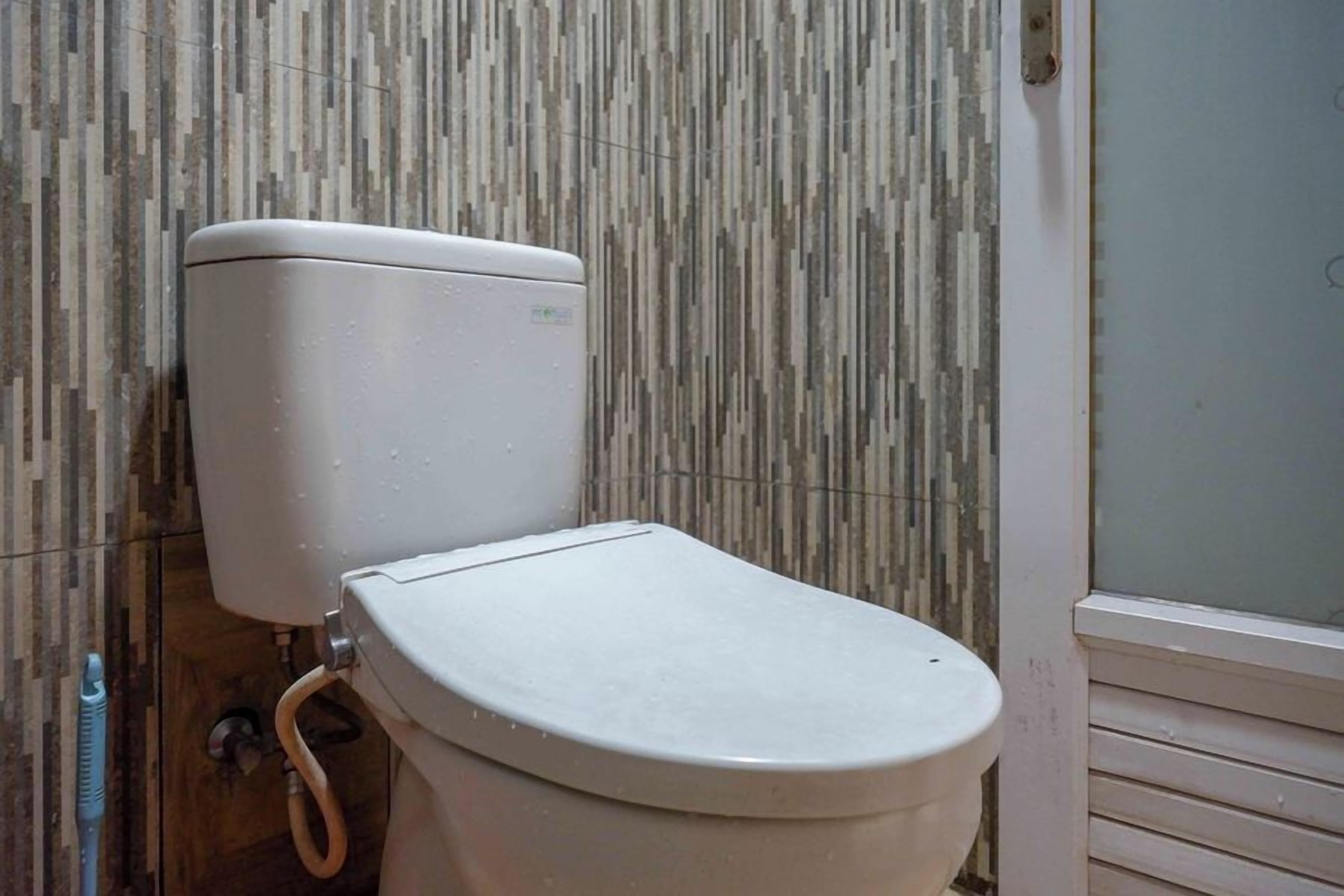 A toilet with a white tank and lid, positioned against a wall with a vertical striped pattern.