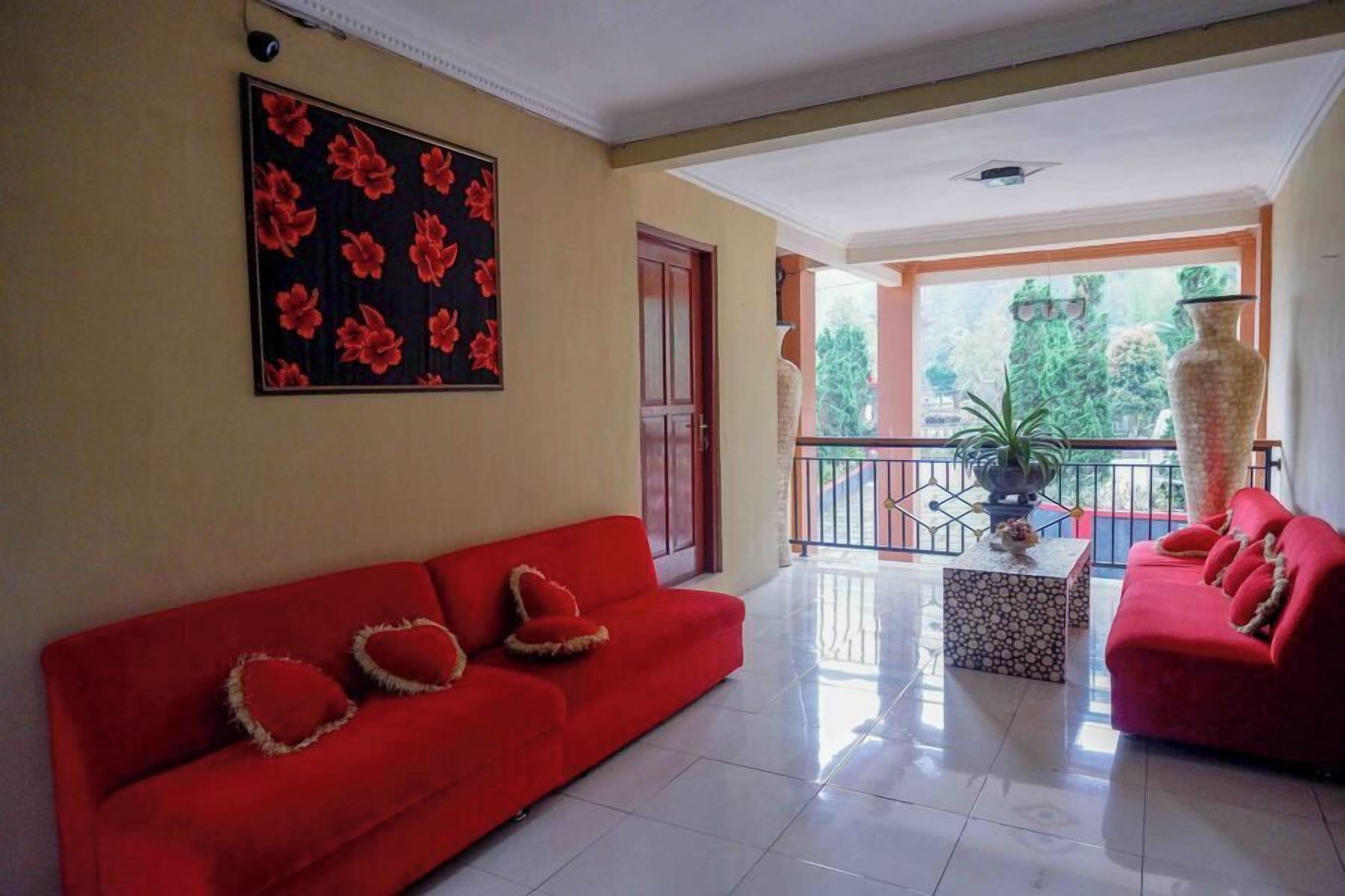 Un salón espacioso con un sofá rojo, un cuadro floral grande y un balcón con vistas a la vegetación.