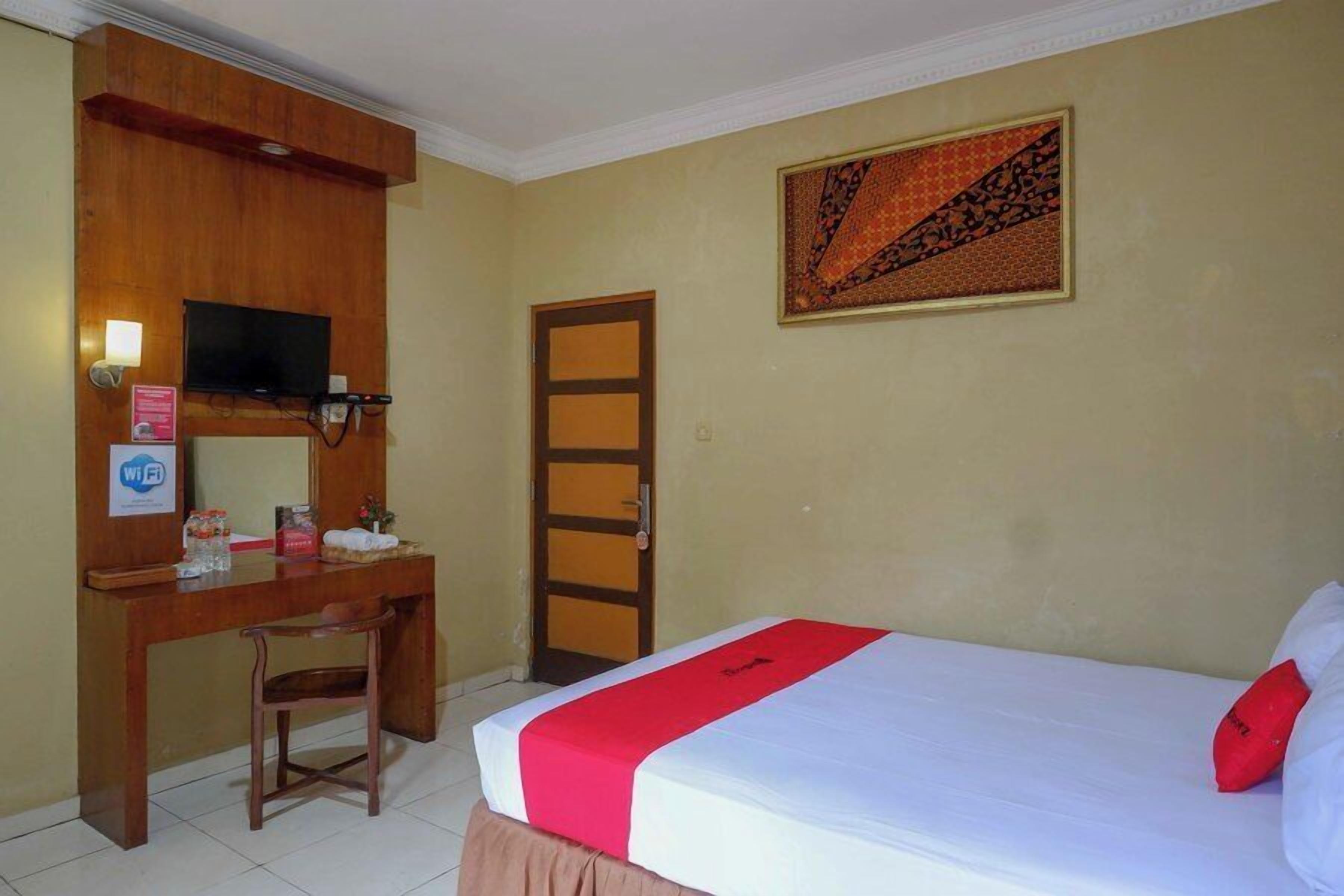 A hotel room with a bed, a desk, a television, and a door.
