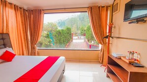 A hotel room with a bed, a desk, a TV, and a window with curtains. - Red Chilies Hill Hotel (Tawangmangu)