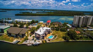 Vue aérienne d’un quartier résidentiel situé sur la côte, avec des maisons, une piscine et un port de plaisance où sont amarrés des bateaux.