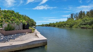 Une rive bordée d’une promenade en béton, d’une végétation luxuriante et sous un ciel bleu dégagé.