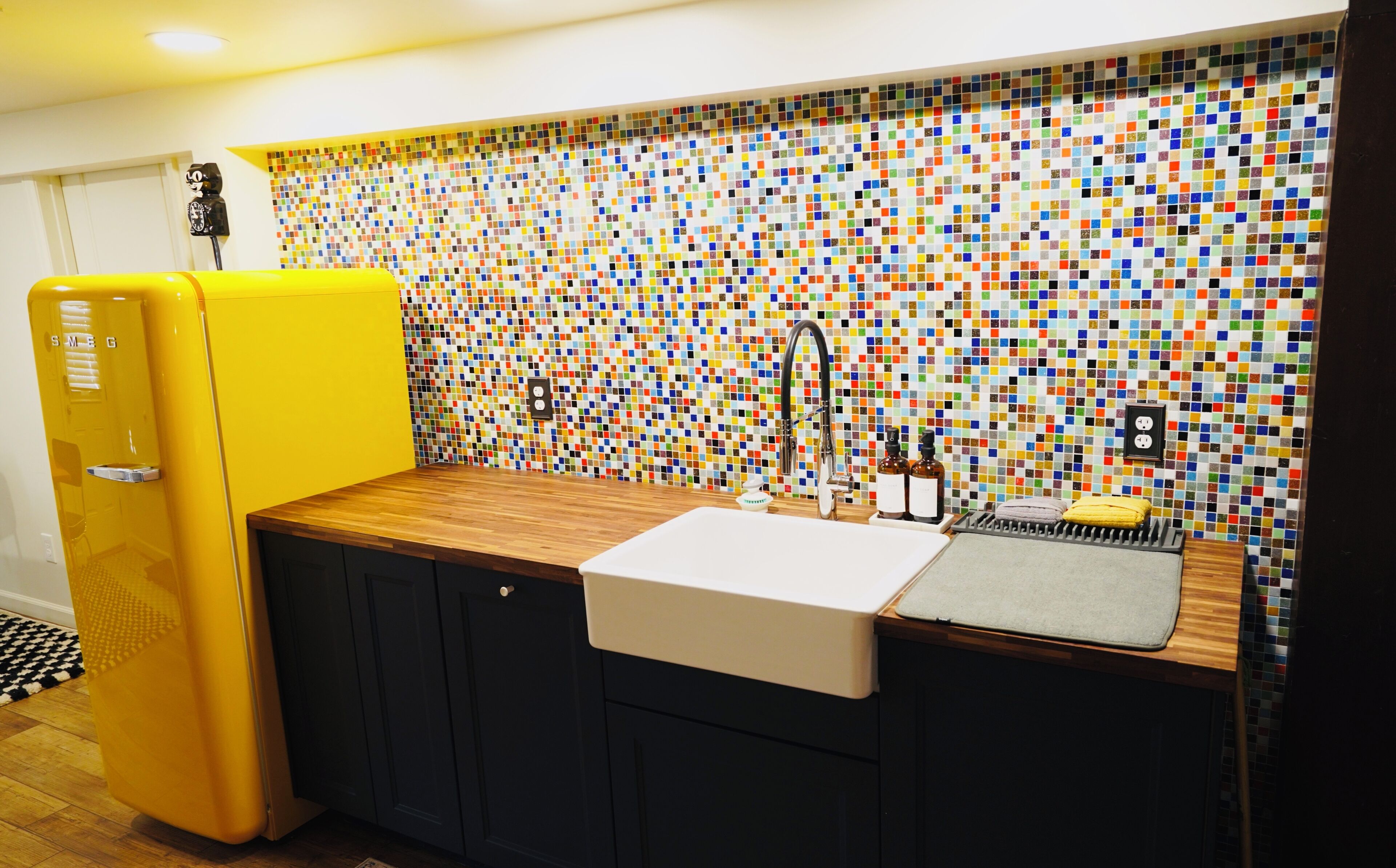 Una cocina moderna con un salpicadero de mosaicos coloridos, un refrigerador amarillo y una encimera de madera.