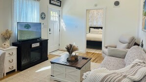 A living room with a TV, a sofa, a coffee table, and a bed in the background.