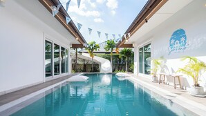 A swimming pool with a slide, surrounded by potted plants and outdoor furniture.