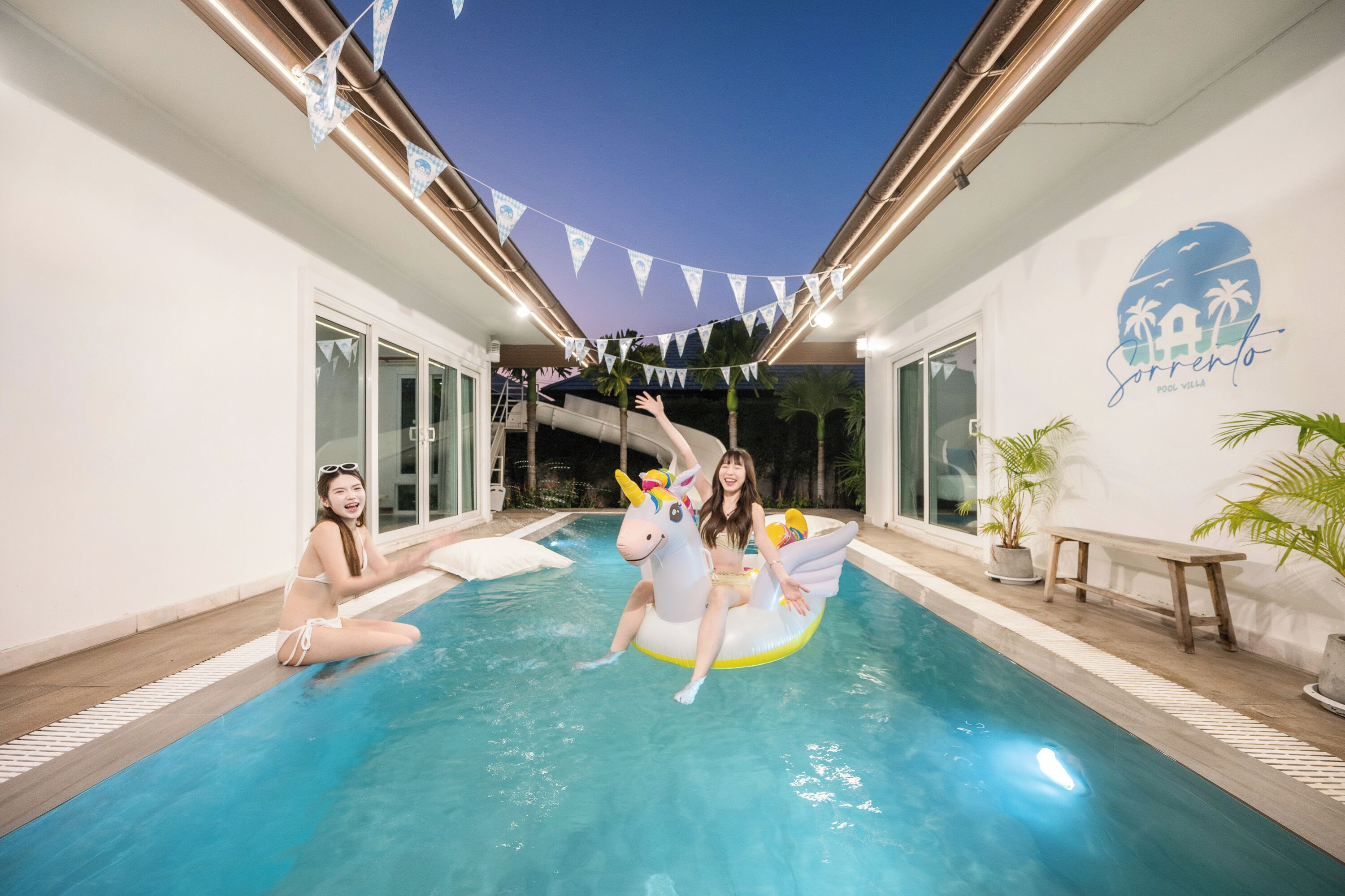 Una piscina interior con un flotador de unicornio, palmeras y un banderín.
