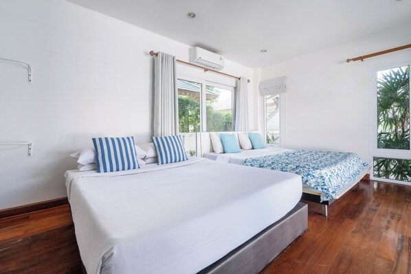 Quarto moderno com duas camas, uma janela grande com cortinas e vista para o verde lá fora.