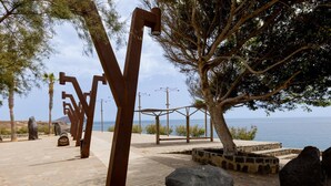 Un chemin de pierres menant à une plage où se trouvent une grande sculpture métallique et un arbre.