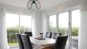 A dining area with a table set for six, surrounded by chairs, large windows, and a view of greenery. - Field View 5-Bed House - free parking (Burton upon Trent, Staffordshire, United Kingdom)