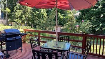 Una terrassa amb taula i cadires, una barbacoa i un parasol.