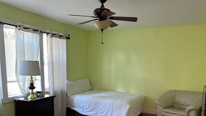Une chambre avec deux lits, un ventilateur de plafond, une lampe et une chaise.