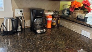 Un plan de travail de cuisine avec une machine à café, une bouilloire, une tasse, un récipient rempli de grains de café et un panier de fleurs.