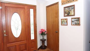 A wooden door with a glass panel, a small table with a vase of flowers, and three framed pictures on the wall.