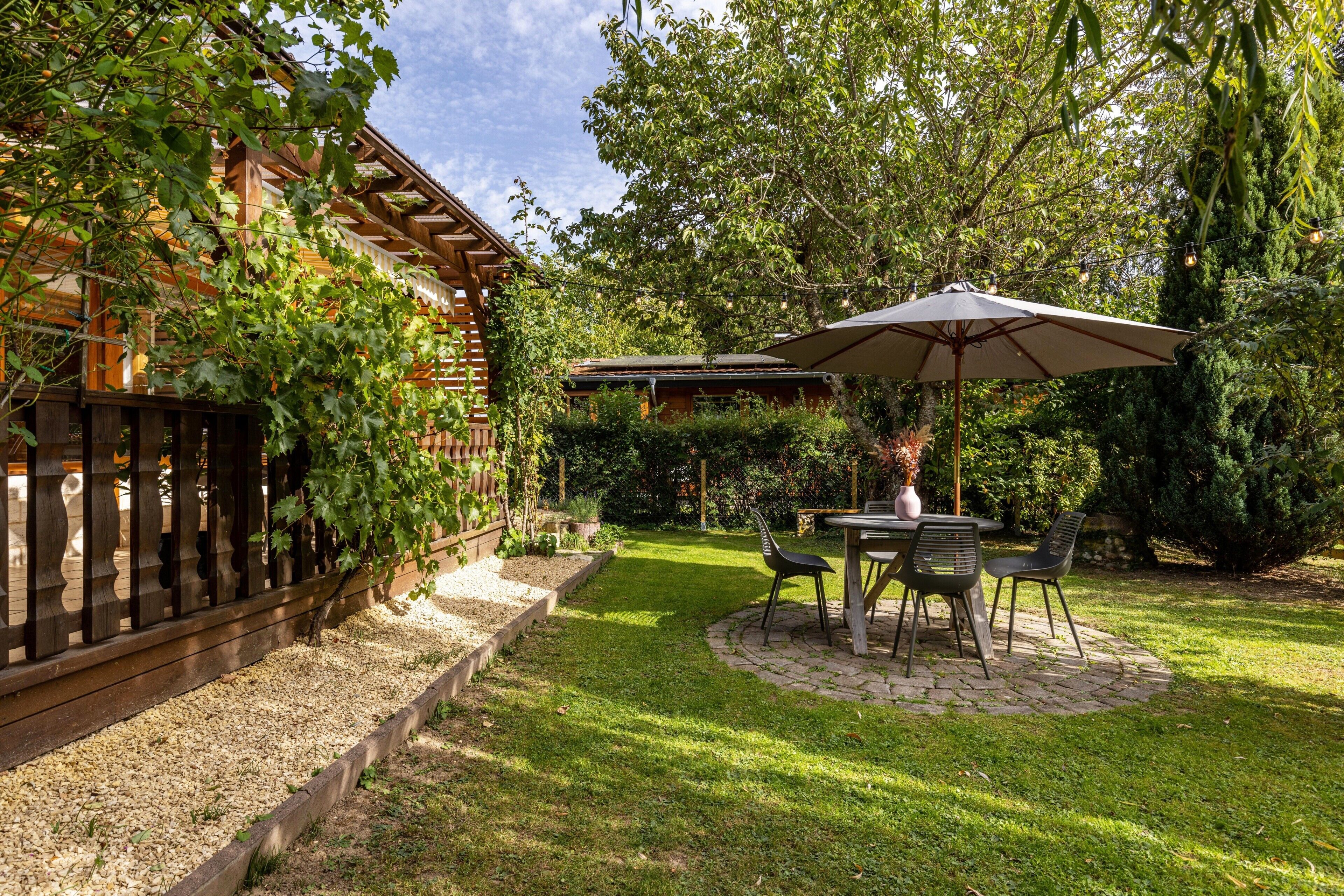 Un patio con mesa y sillas, rodeado de un jardín con valla de madera y follaje.