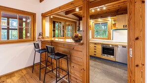 Une cuisine avec des poutres en bois, un coin bar avec des tabourets et une vue sur la verdure à l’extérieur.