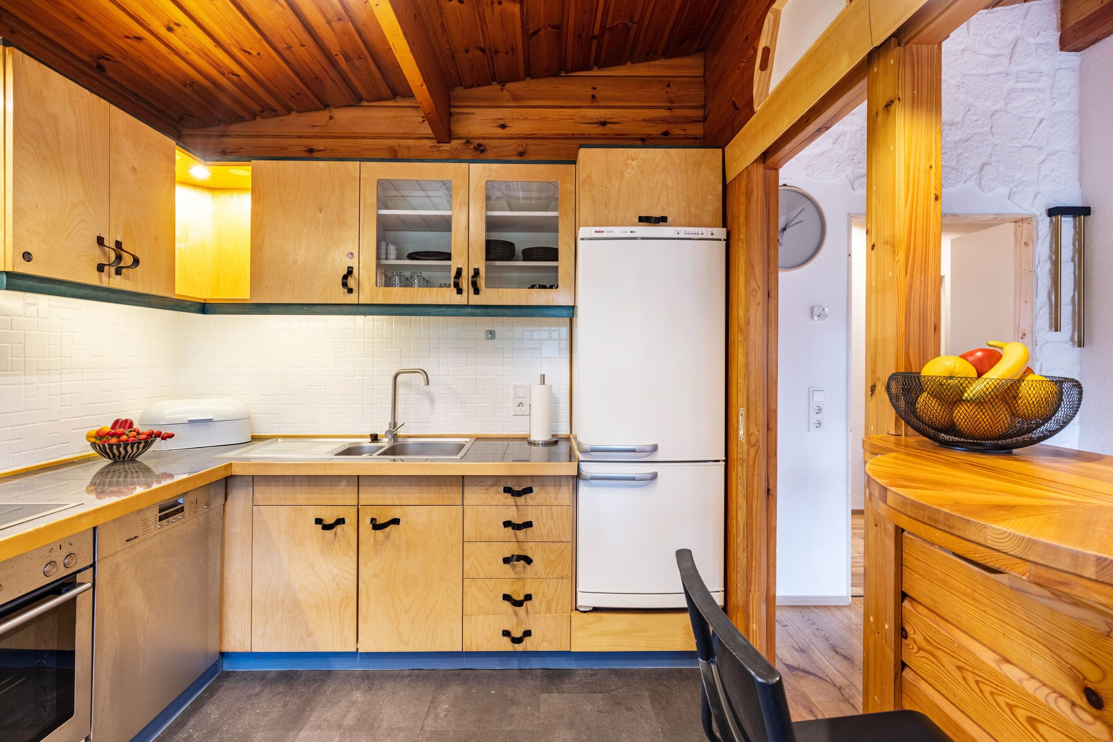 Eine Küche mit Holzausstattung, einem weißen Kühlschrank, einer Spüle und einer Fruchtschale auf der Arbeitsplatte.
