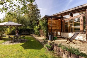 Un patio con mesa y sillas, una pérgola de madera y un jardín con plantas y una cerca de madera.