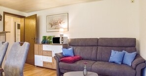 Uma sala de estar com sofá, mesa lateral, luminária, televisão e aparador.