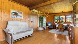 A wooden interior with a white leather sofa, a dining table with chairs, and a kitchen area with cabinets and a stove.