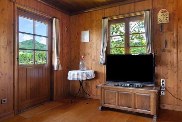 A wooden-paneled room with a television on a wooden cabinet, a table with a striped tablecloth, and a window with curtains.