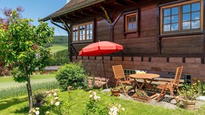 A wooden house with a garden, outdoor seating, and a red umbrella.