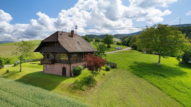 A traditional house with a sloped roof, surrounded by lush green fields and a clear sky.