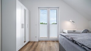 Un dormitorio con cama, escritorio, silla y puerta corredera a un balcón.
