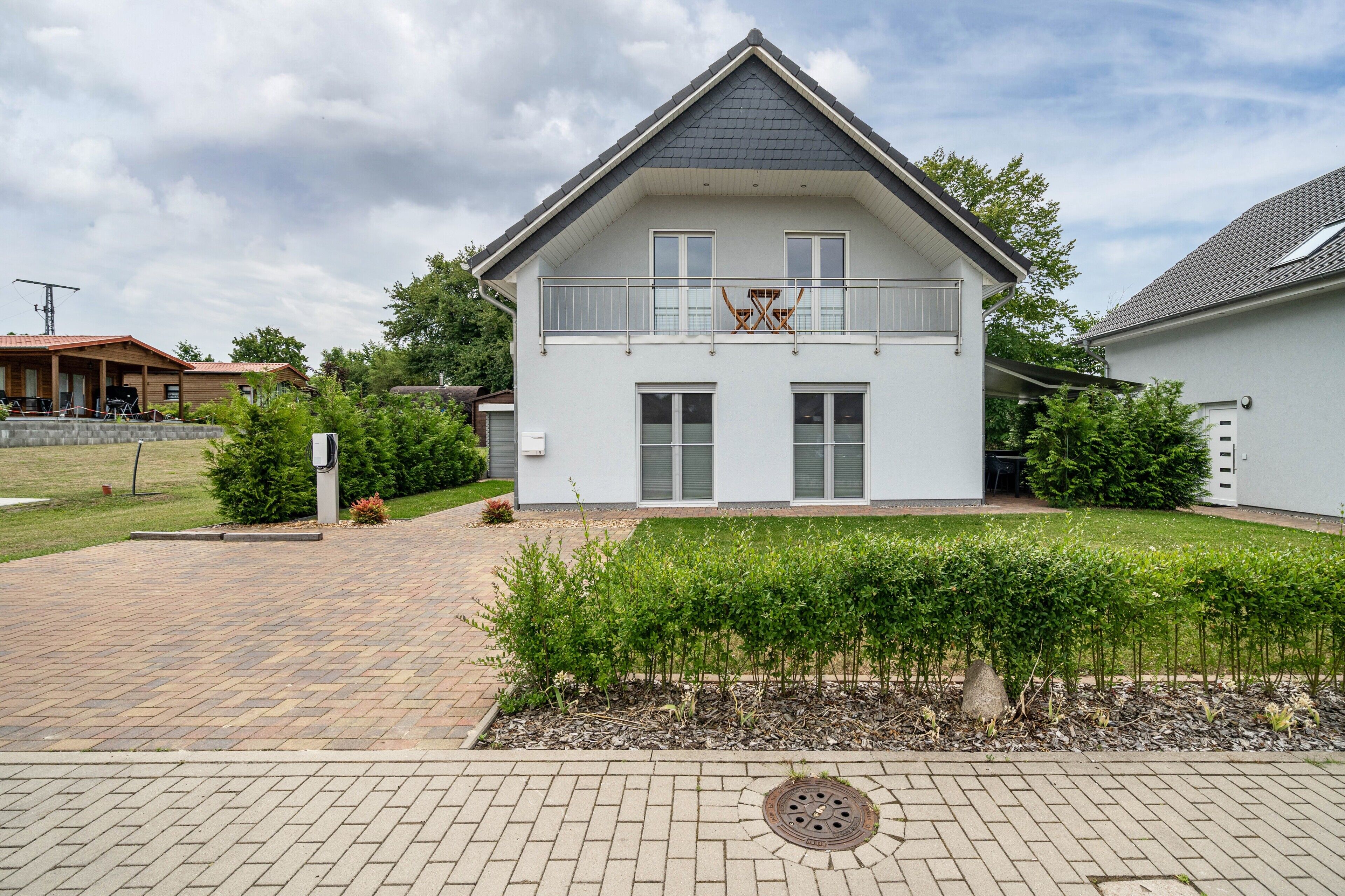 A two-story house with a balcony, a paved driveway, and a well-maintained garden.