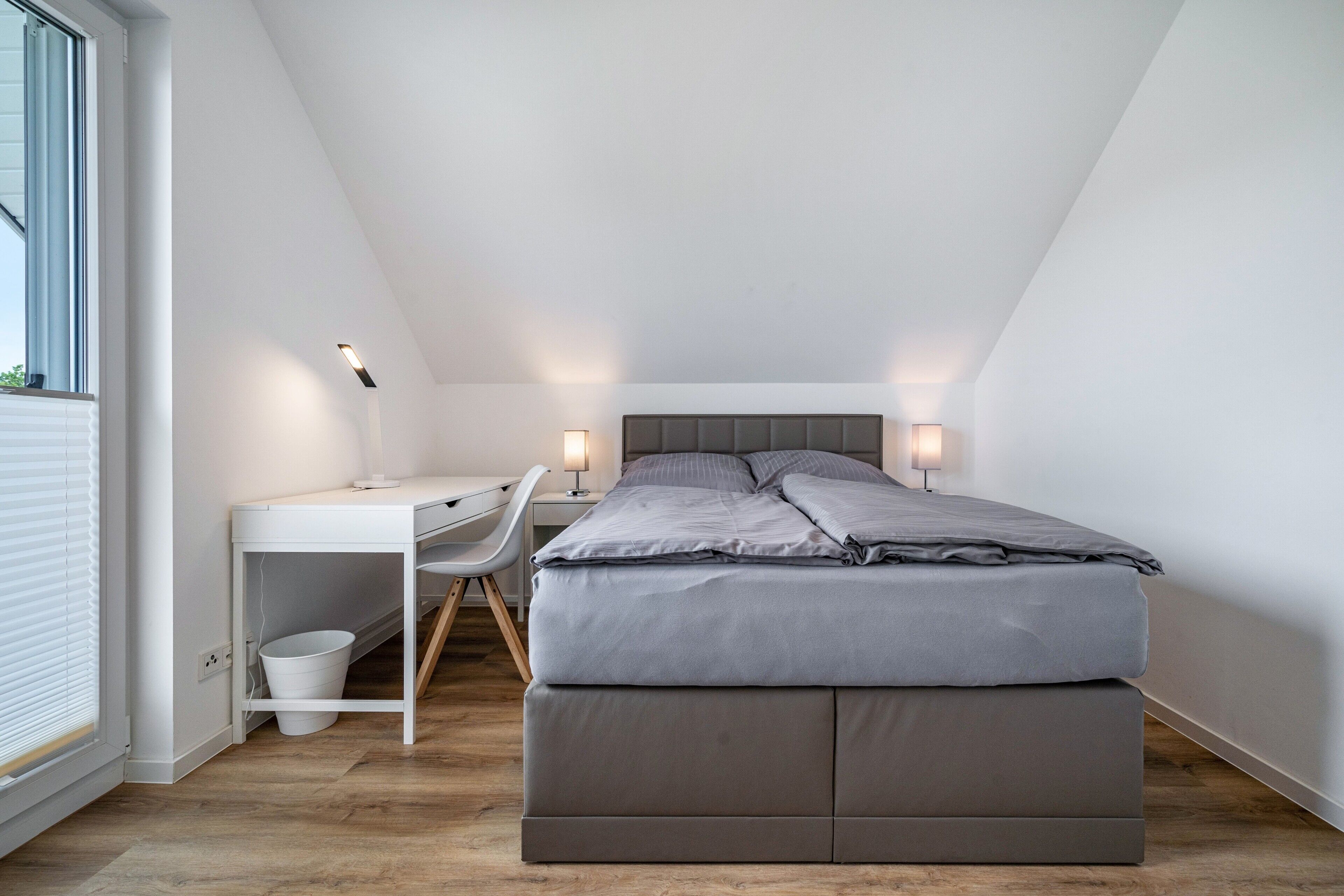 Un dormitorio con cama, escritorio, silla y lámparas de noche.
