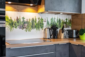 Ett kök med modern design, med en bänkskiva i trä, en vattenkokare i rostfritt stål, en brödrost och ett knivställ.