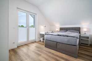 Un dormitorio con cama, mesitas de noche, un escritorio y una ventana con persianas.