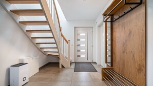 Un pasillo con una escalera de madera, un radiador blanco, un felpudo negro en la puerta y un banco de madera.