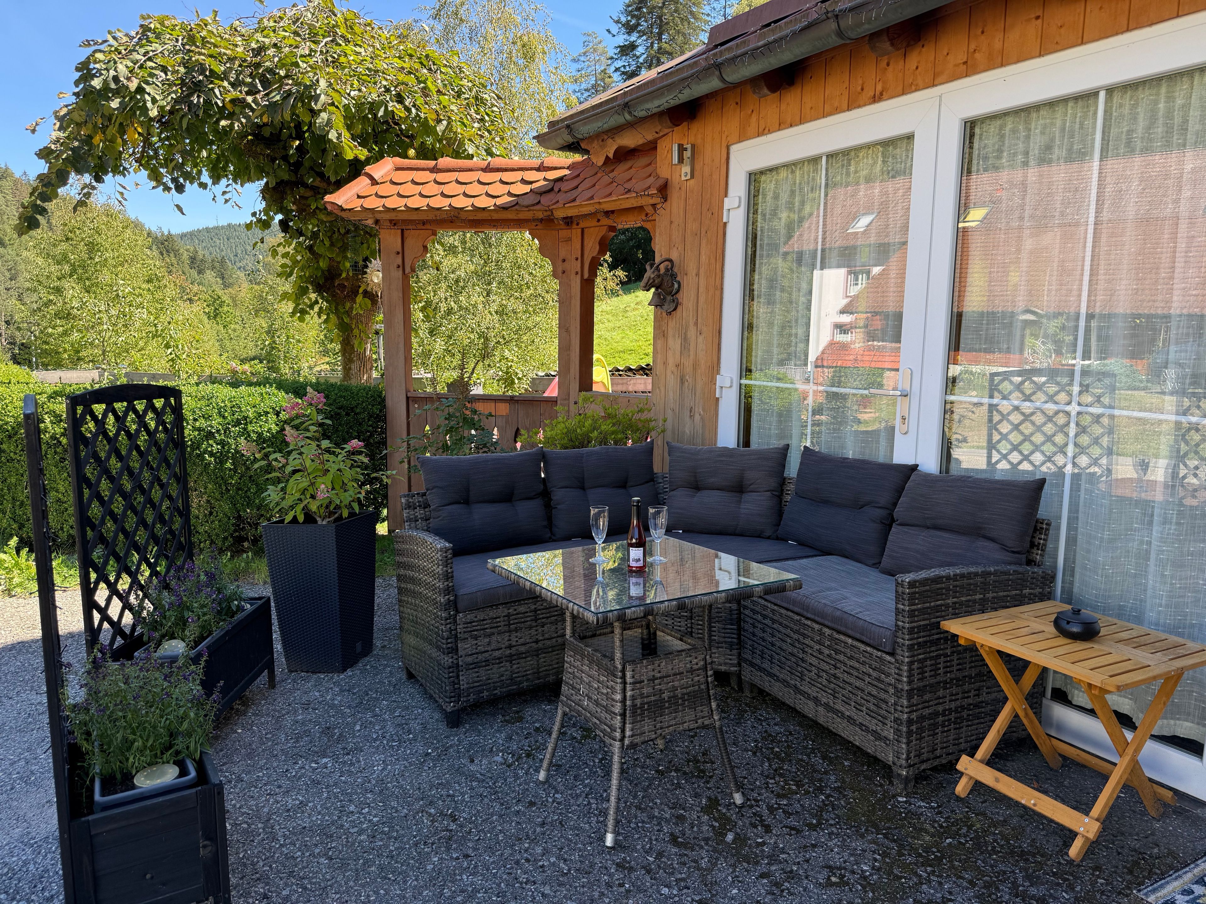 Ulkoterassi, jossa on punottuja huonekaluja, lasipöytä ja pergola.