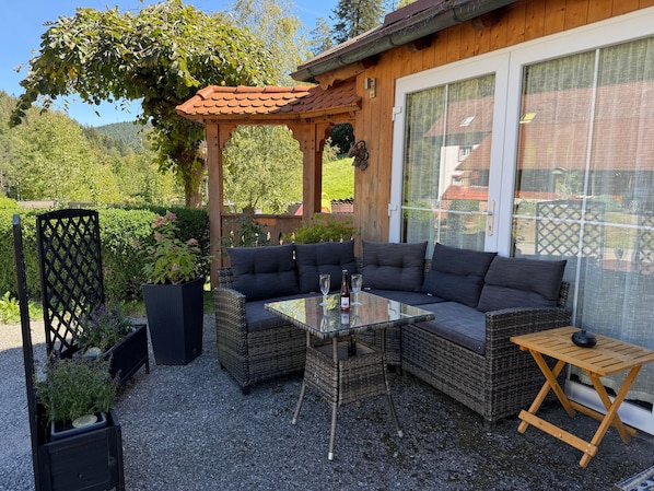 An outdoor seating area with wicker furniture, a glass table, and a pergola.