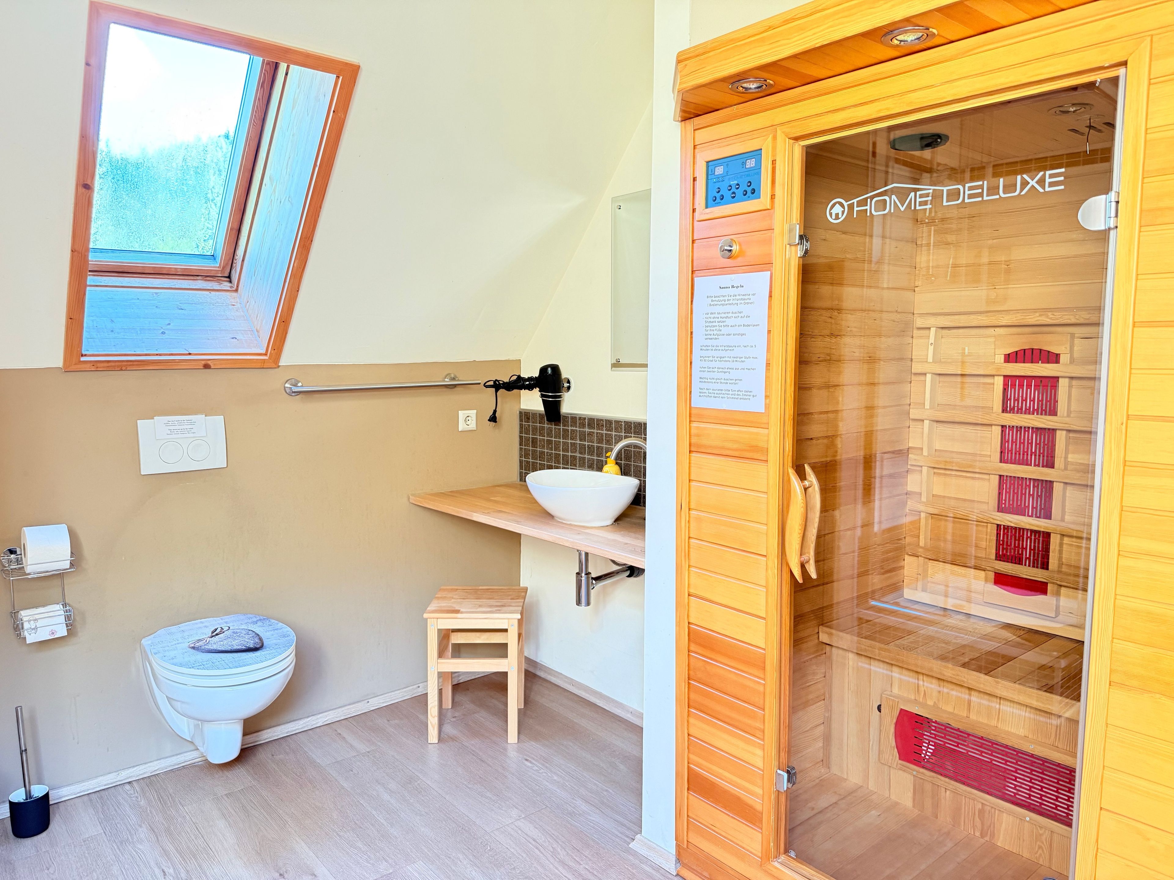 A bathroom with a skylight, a toilet, a sink, a small wooden stool, and a sauna.