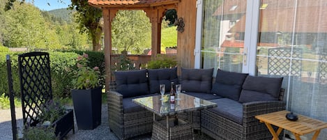Ein Außenbereich mit Korbmöbeln, einem Glastisch und einer Pergola.