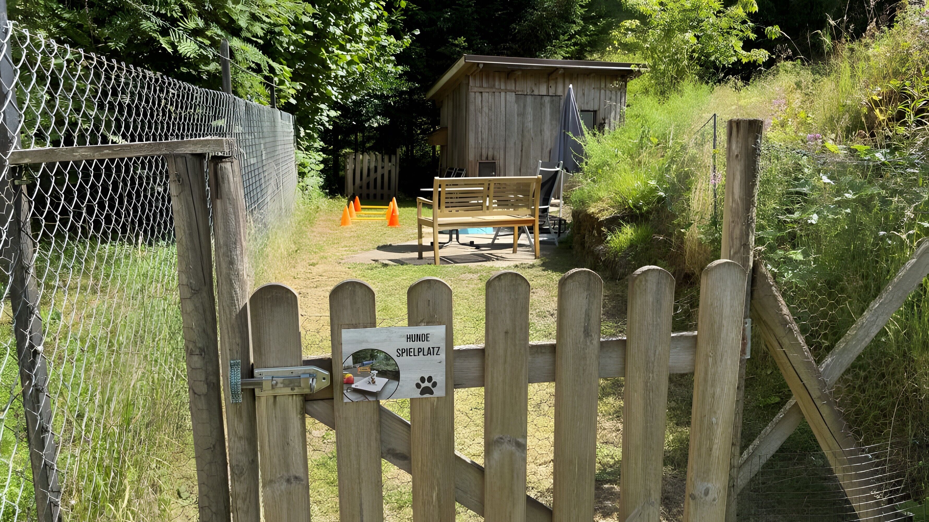 A wooden gate with a sign indicating a dog play area, a wooden bench, and a small wooden structure in the background.