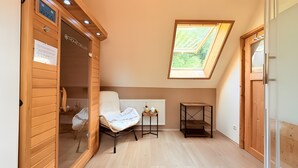 Una habitación con cama, una mesita, un radiador, una ventana con vistas y puertas de madera.
