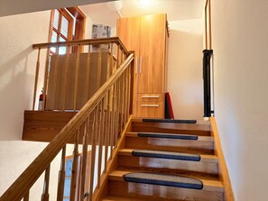 Una escalera de madera con barandal, una puerta de madera y una lámpara fijada a la pared.