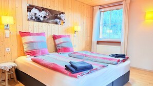 A wooden-paneled room with a bed, two wall-mounted lamps, a window with curtains, and a small stool. - Holiday Apartment 'Waldblick' with Fireplace, Fenced Garden, Playground, Grill, Wi-Fi, Sauna (Enzklösterle)