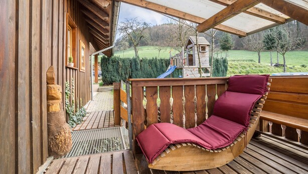 Una terraza de madera con un banco de madera y una casita de juegos con tobogán al fondo.